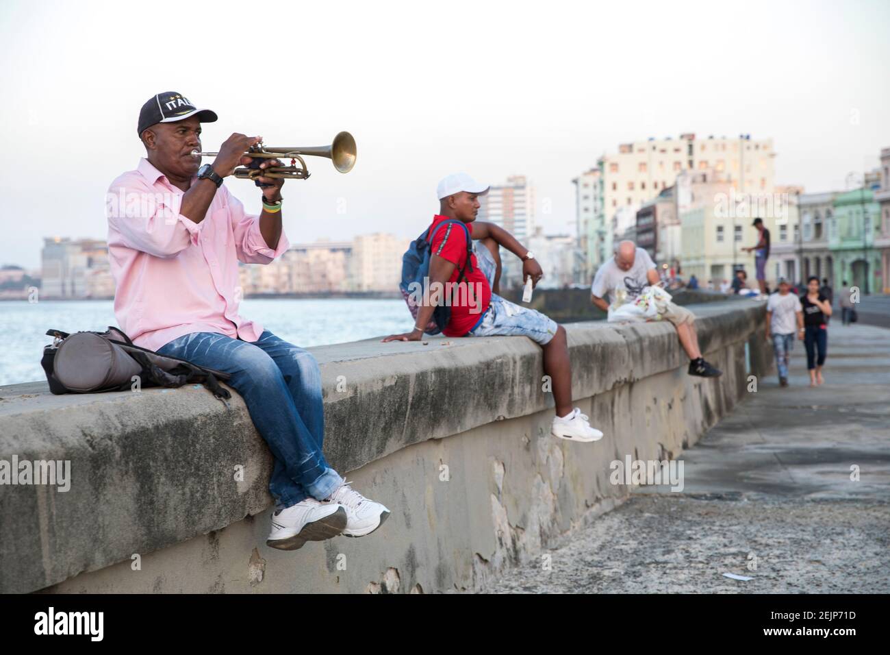 An older man, sitting on the Malecon wall in Havana, plays the trumpet Stock Photo