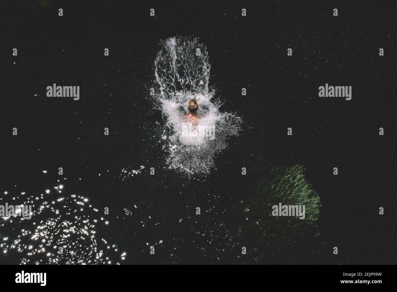 Blonde Boy Jumps and Lands in a Dark Pool Creating Big Splash Stock