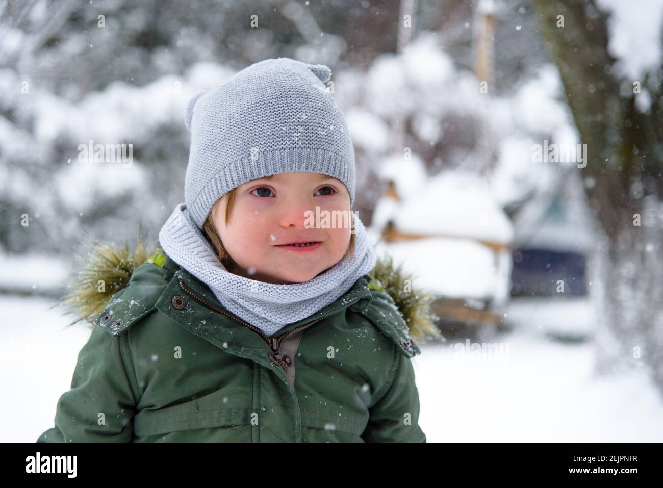 Down syndrome toddler boy in a winter outfit, a warm grey scarf in a green  jacket gloves enjoys the frosty winter weather and snow. Winter fun in the  Stock Photo - Alamy