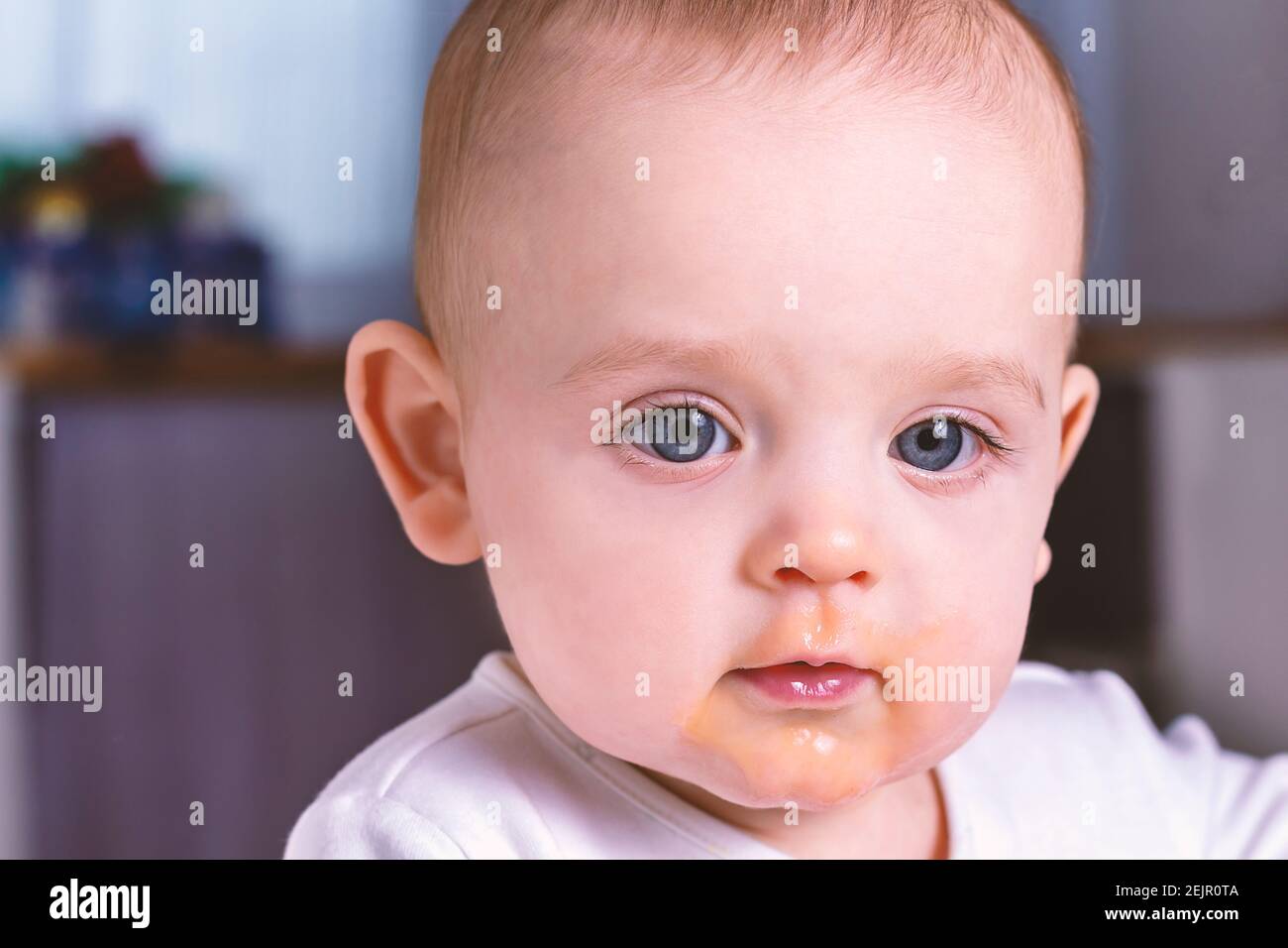 Small caucasian baby with dirty face after eating. First baby fruit puree. Close up photo of caucasian baby boy. Child learning to eat.  Stock Photo
