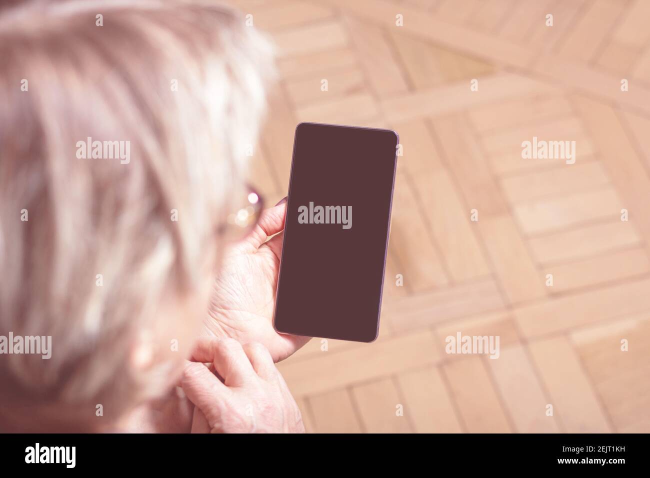 Elderly womans hand holding mobile cell phone. Over shoulder. Old woman looking at cell phone. Close-up. Blanck mobile phone screen. Display media.  Stock Photo