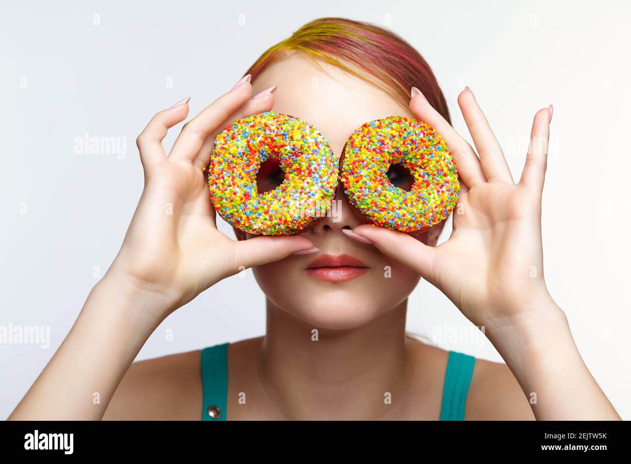 Teenager girl with unusual face art make-up . Child with donuts in hands closing eyes and looking through holes in donuts. Sweet tooth concept. Stock Photo