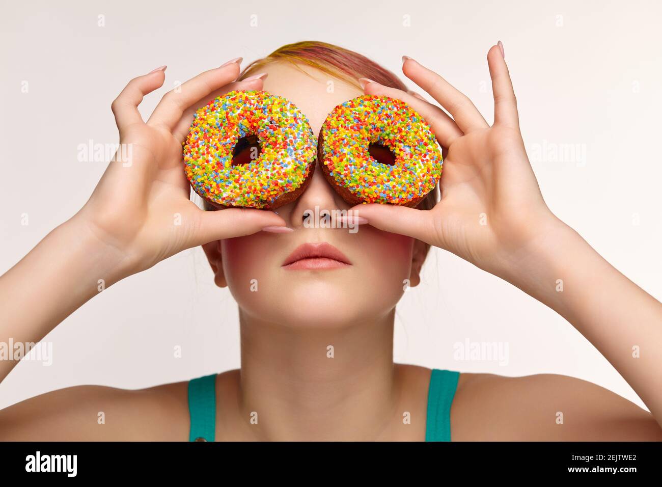Teenager girl with unusual face art make-up . Child with donuts in hands closing eyes and looking through holes in donuts. Sweet tooth concept. Stock Photo