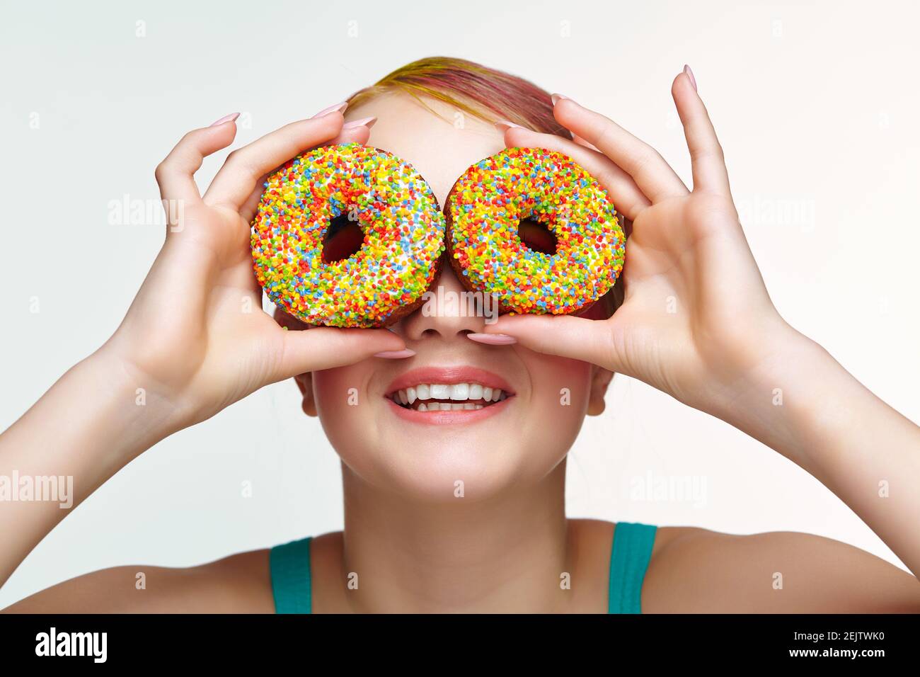 Teenager girl with unusual face art make-up . Child with donuts in hands closing eyes and looking through holes in donuts and smiling. Sweet tooth con Stock Photo