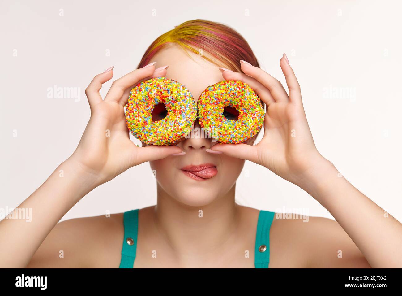 Teenager girl with unusual face art make-up . Child with donuts in hands closing eyes and looking through holes in donuts and showing tongue. Sweet to Stock Photo