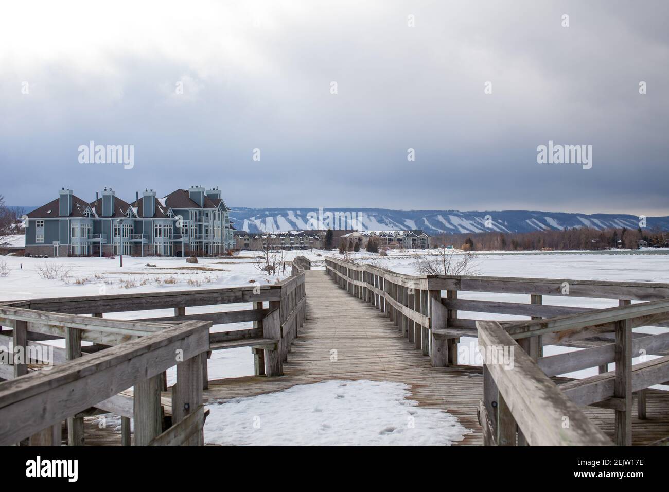A wooden bridge in Lighthouse Point, Collingwood, crosses a portion of Georgian Bay while overlooking the Blue Mountain Ski hills from a distance, wit Stock Photo