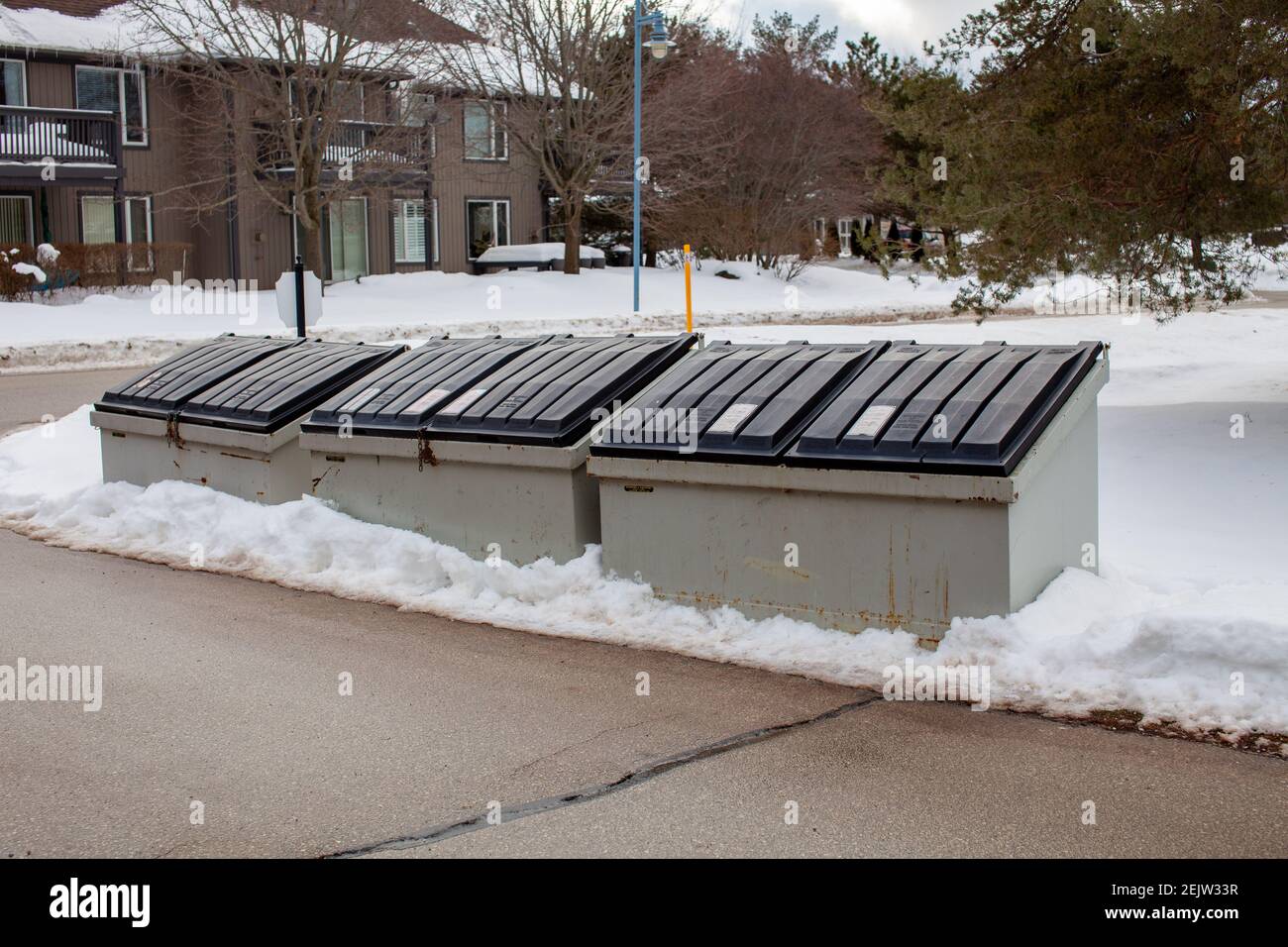 Three large metal garbage bin sits on the side of a street in a condo corporation for residents