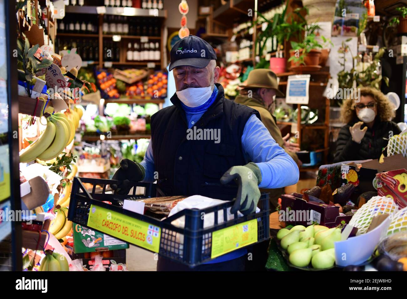 Milan, Italy - 13 March 2020: Roberto , the owner of the greengrocer shop  Frutteto Ciovasso in the Brera district, wears a face mask and works as  restrictive measures are taken to