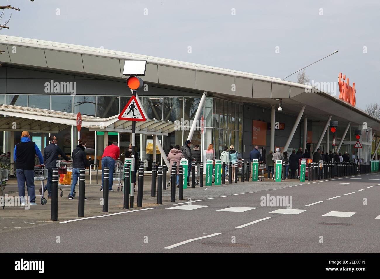 Shoppers queue for their grocery shopping outside Sainsburys in Beckton