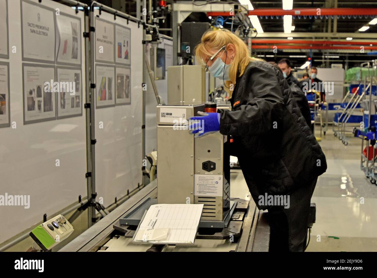 A female assembly operator protected with a surgical mask and gloves ...