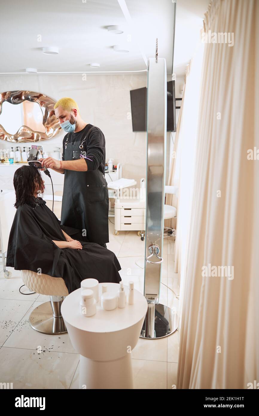 Concentrated stylist blowdrying his client hair with a paddle brush