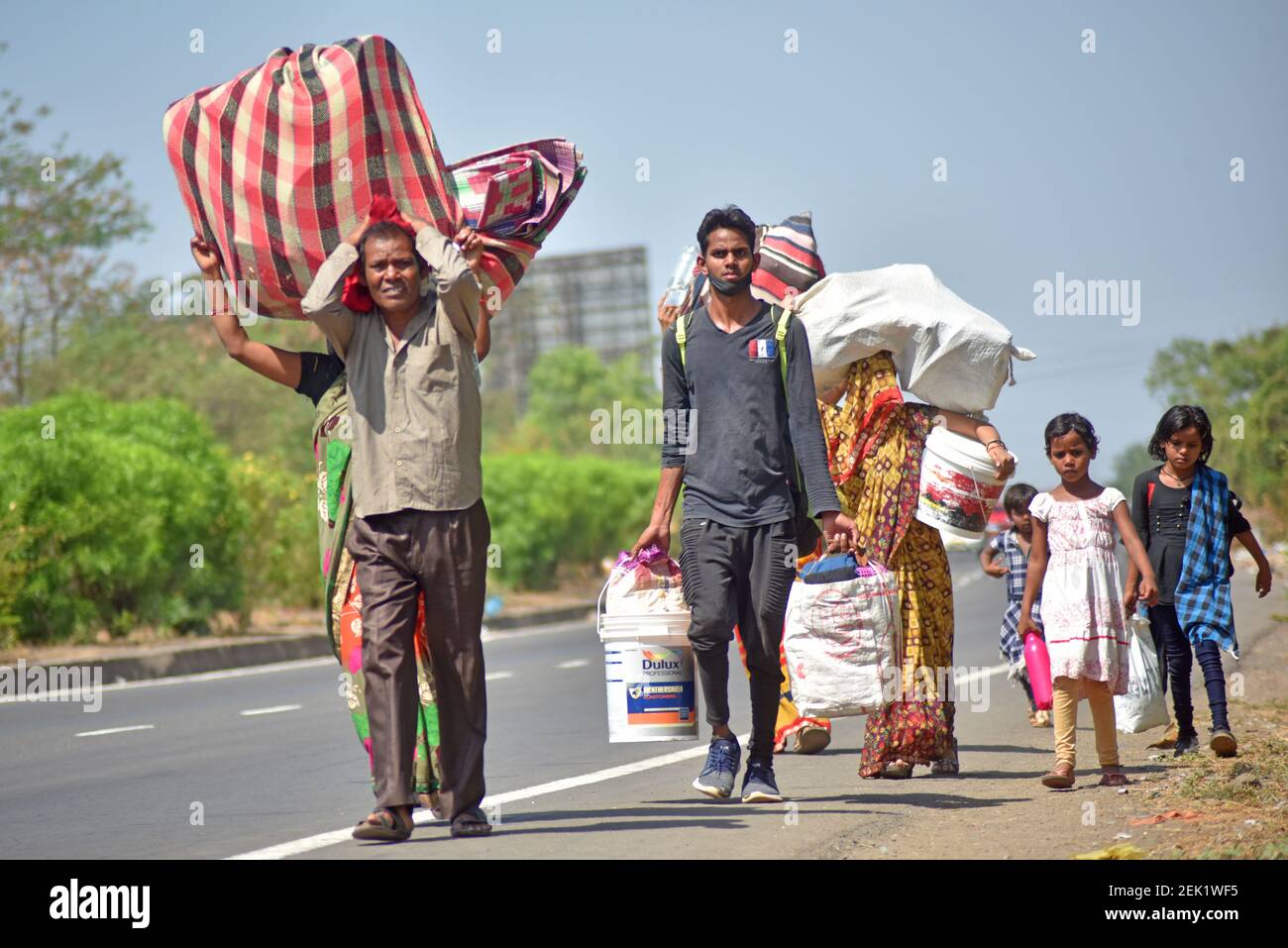 Migrant workers walk along a deserted road while carrying their luggage