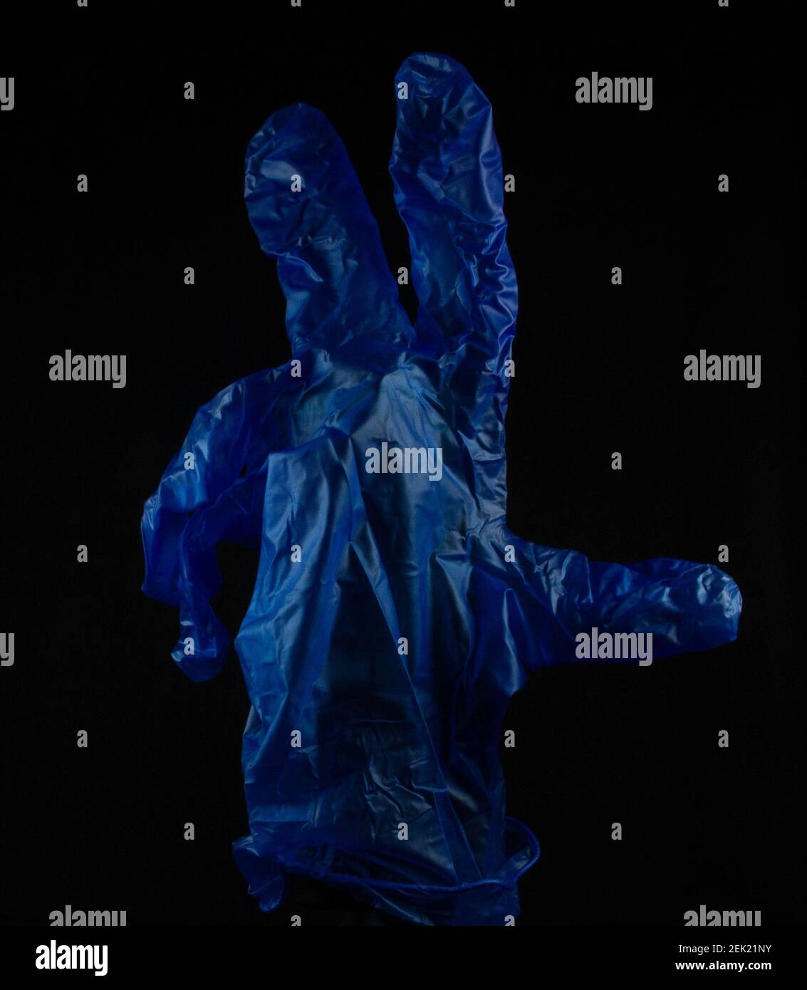 isolated blue latex inspection glove with two fingers raised on a stand on a black background