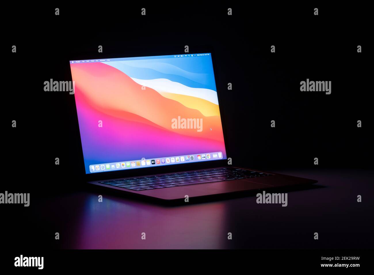 The new MacBook Air with Apple's M1 chip and the latest macOS Big Sur isolated on a desk in the dark. Stock Photo