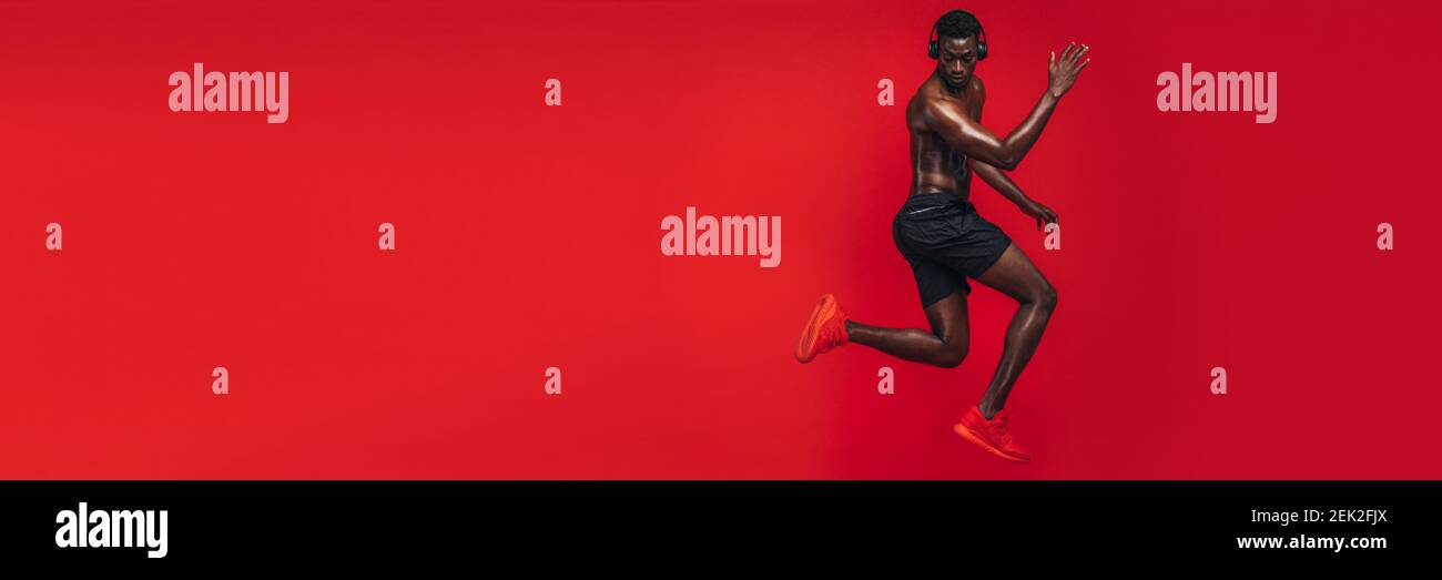 Fit african man exercising in studio with lots of copy space. African american man with muscular body working out on red background. Stock Photo