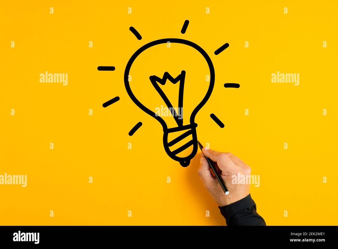 A hand sketching a light bulb on a vibrant yellow background, symbolizing the birth of ideas under focused illumination