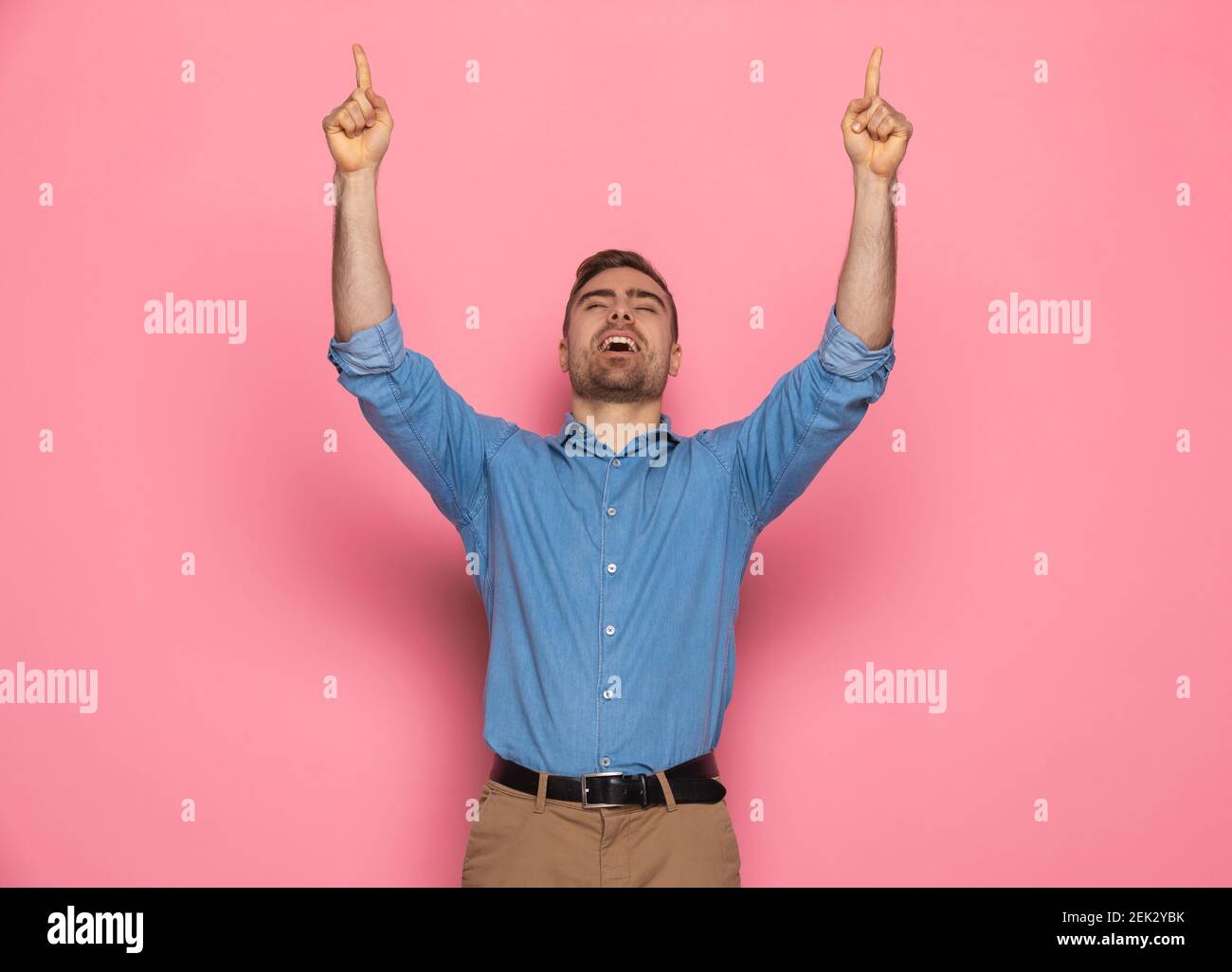 casual young guy in denim shirt holding arms above head, pointing