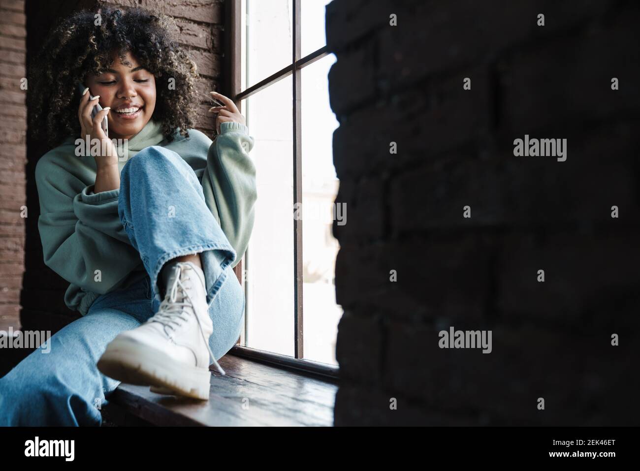 Joyful african american woman talking on mobile phone while sitting on ...