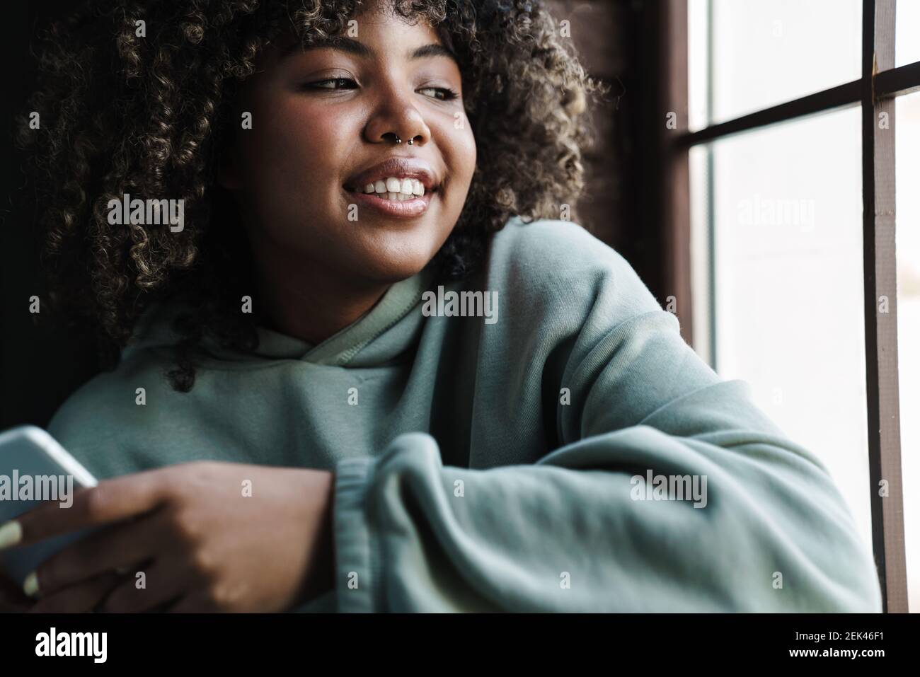 Joyful african american woman using mobile phone while sitting on ...