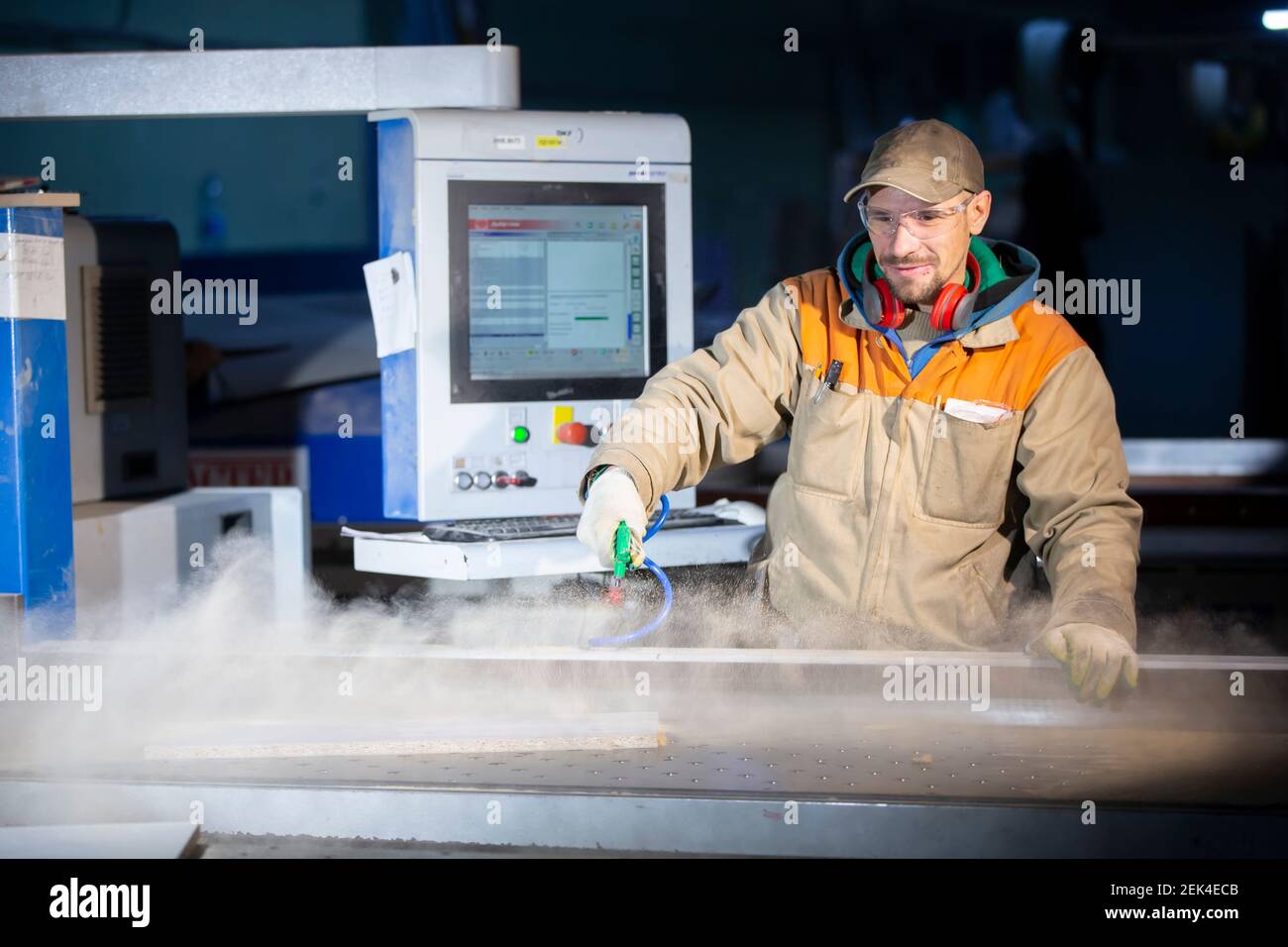 A furniture production worker behind a programmed machine makes furniture parts. Furniture manufacturing. Stock Photo