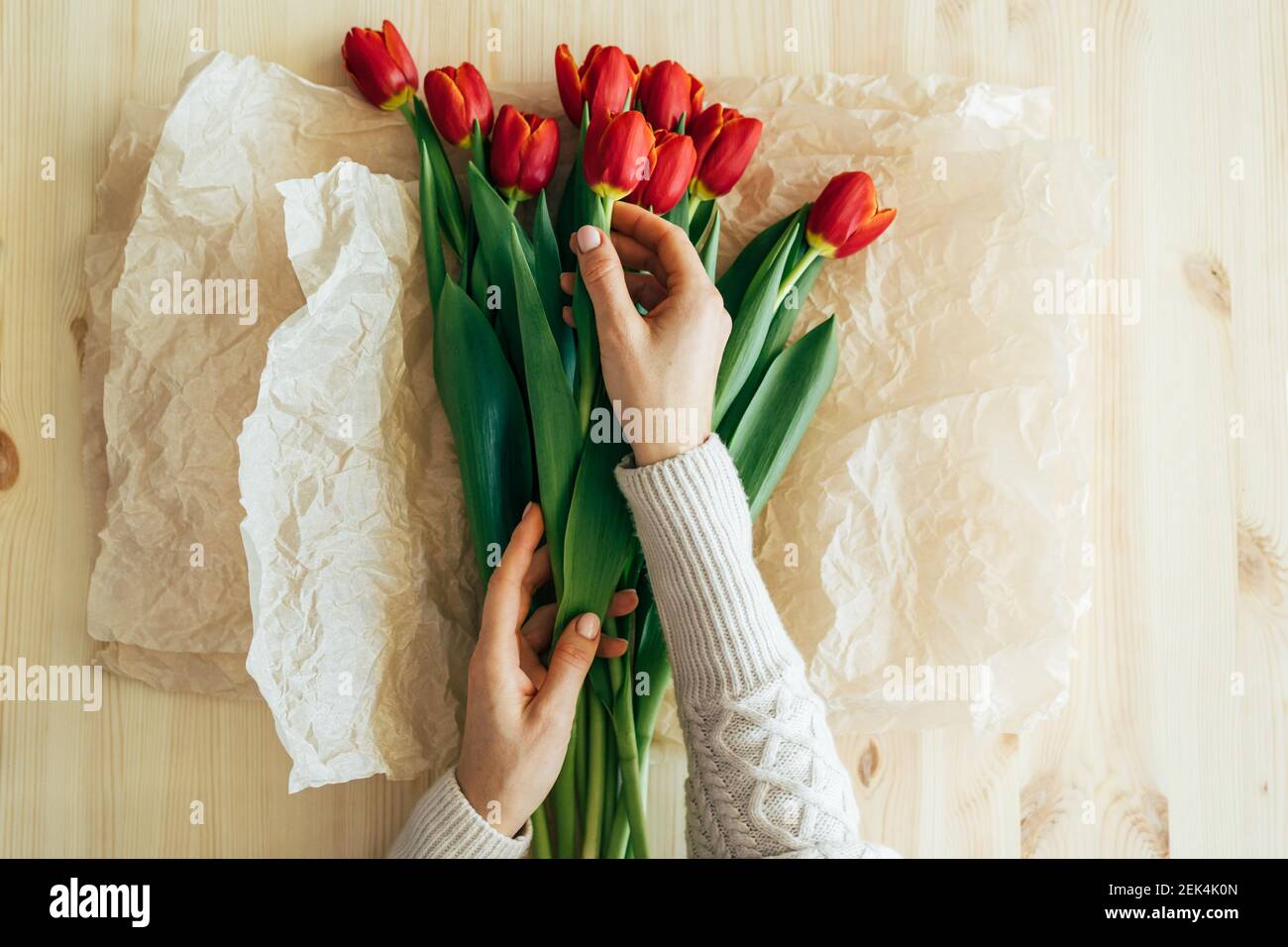 Top view of hands wrapping red tulips in craft paper. Stock Photo