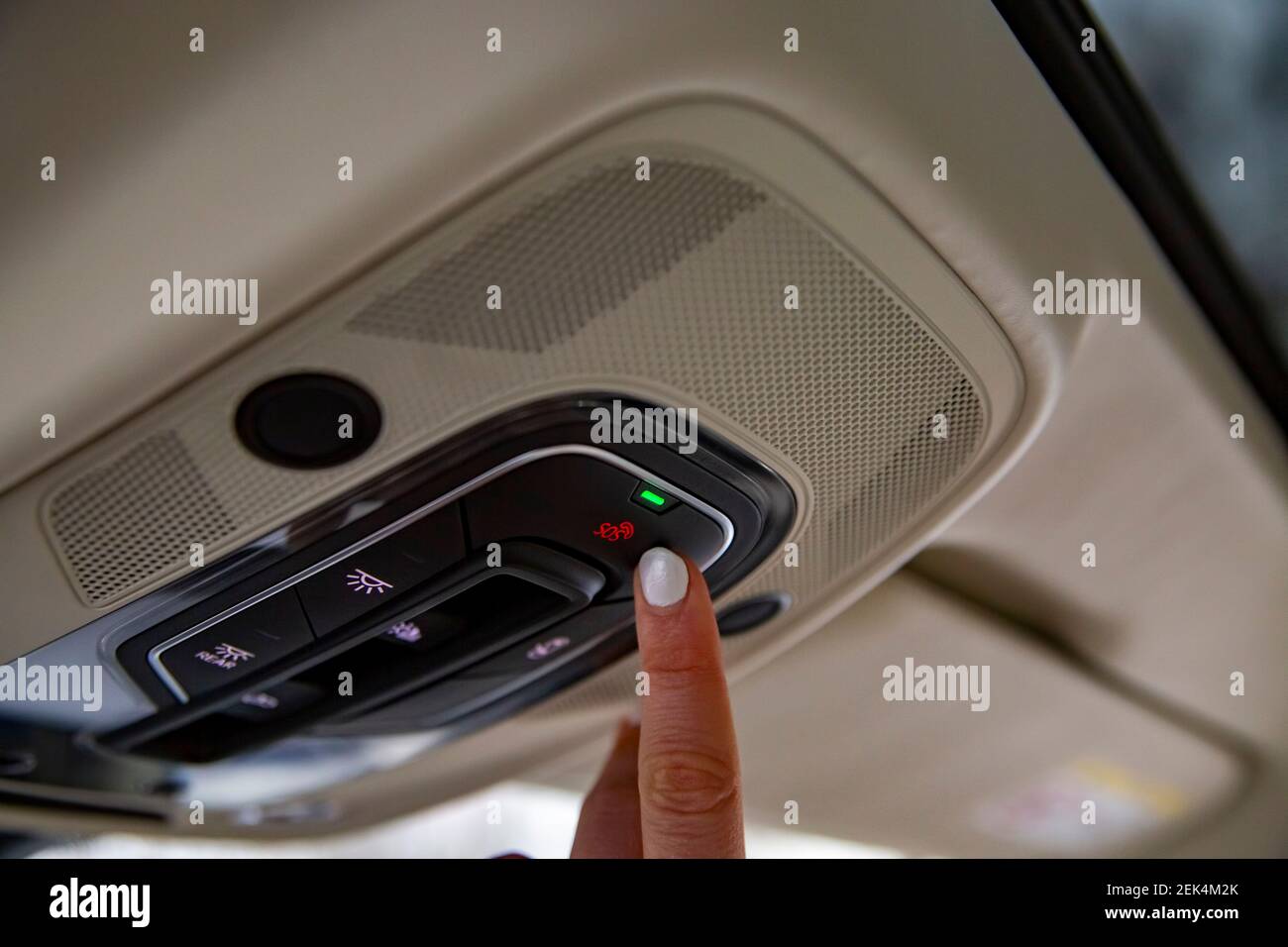 female driver's finger presses sos button on the ceiling panel of a modern car Stock Photo