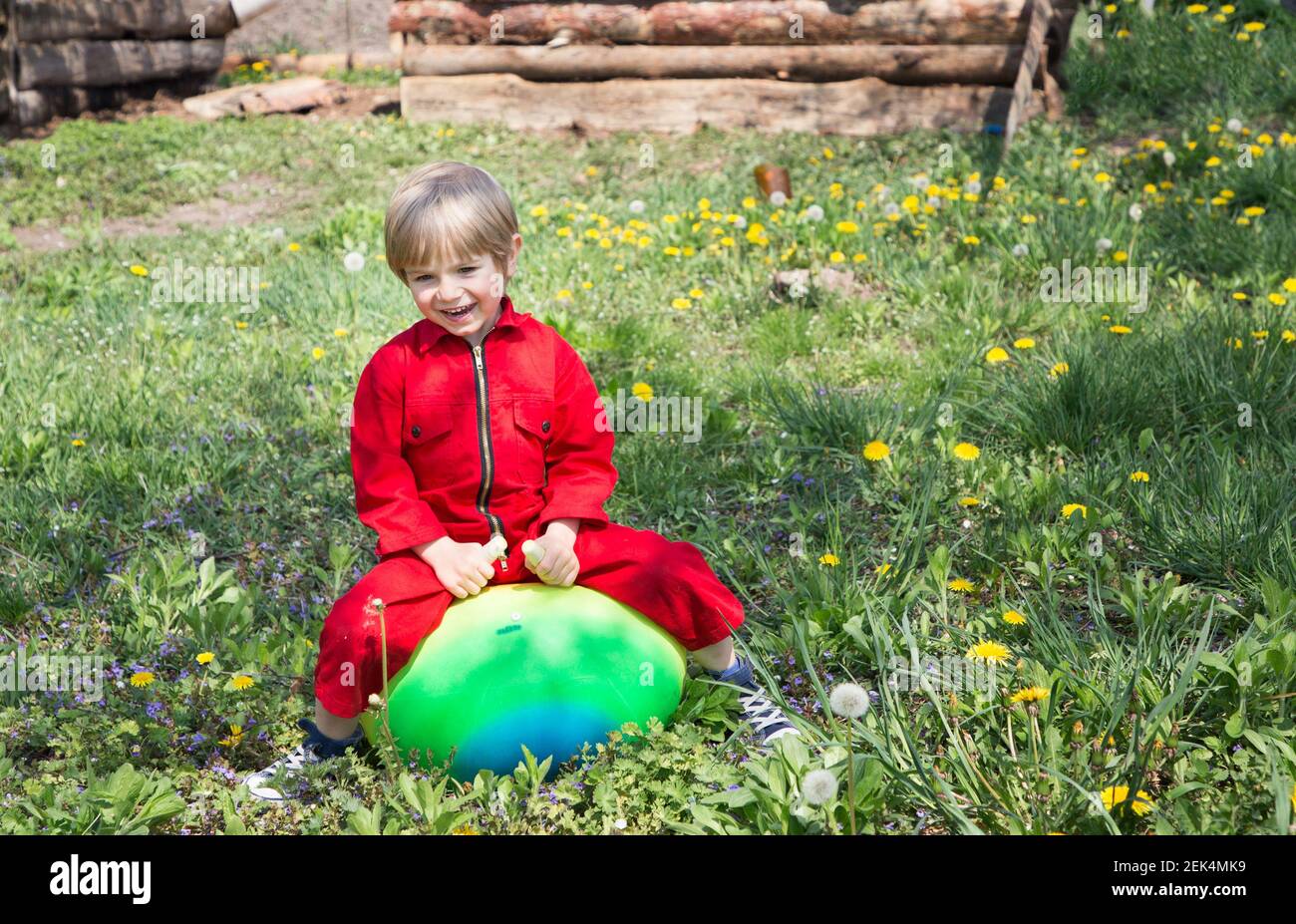 Toddler boy cheerfully jumps on an inflatable ball on green lawn in daytime. Happy childhood, joy of playing outdoors on a warm spring sunny day, free Stock Photo
