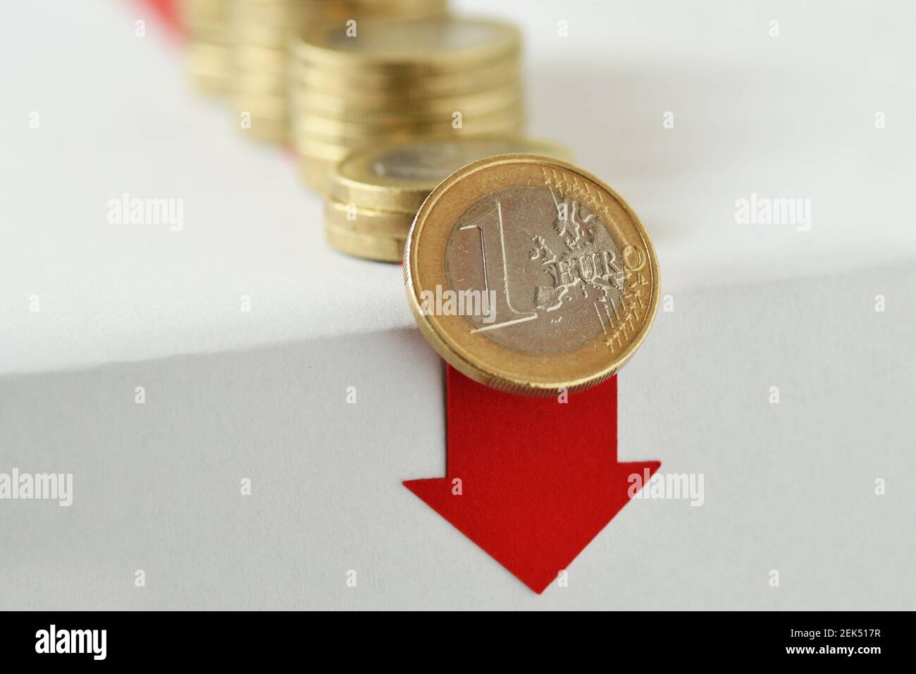 Piles of coins falling down with red arrow - Loss of money concept Stock Photo
