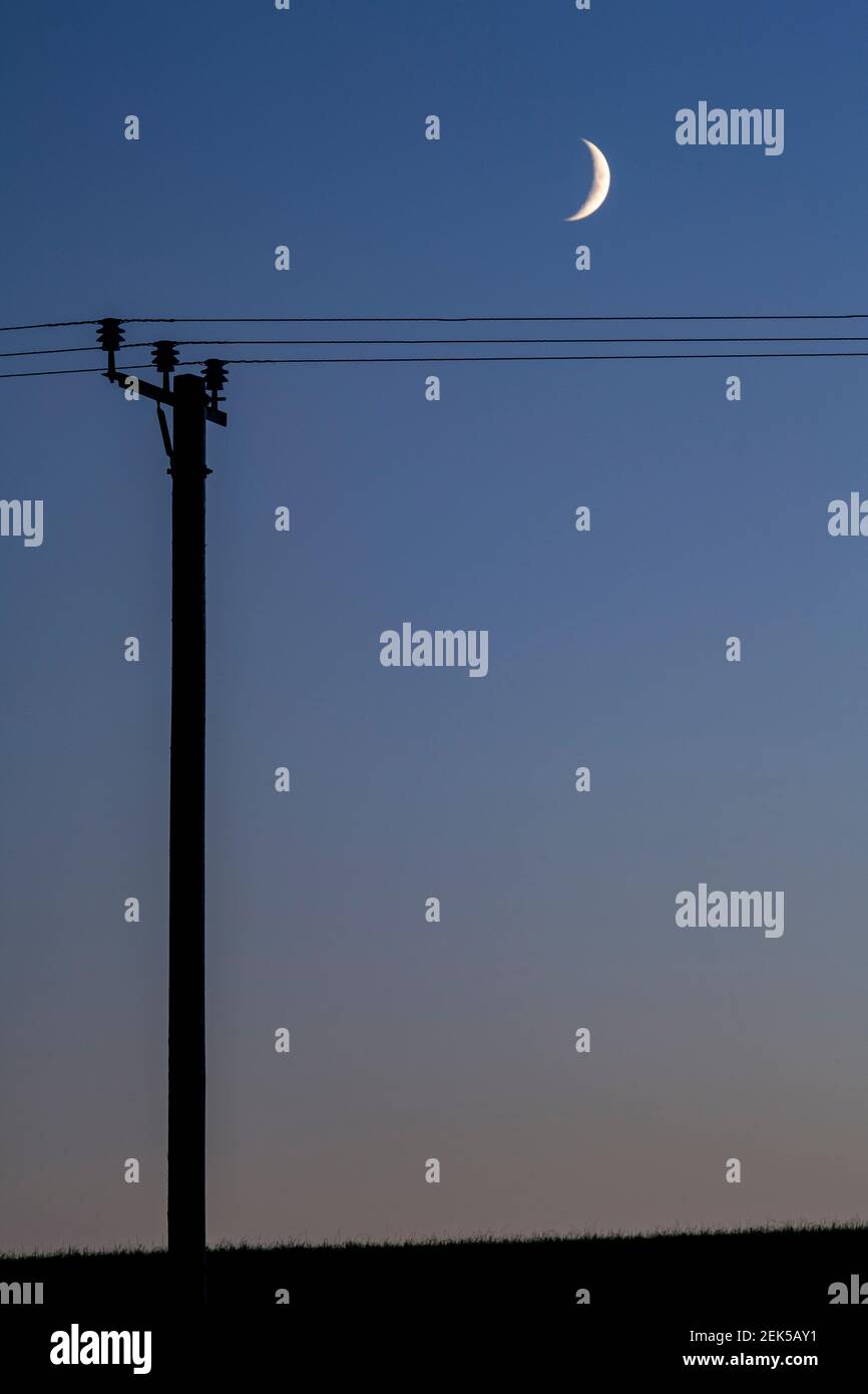 Crescent moon and telegraph pole at dusk Stock Photo