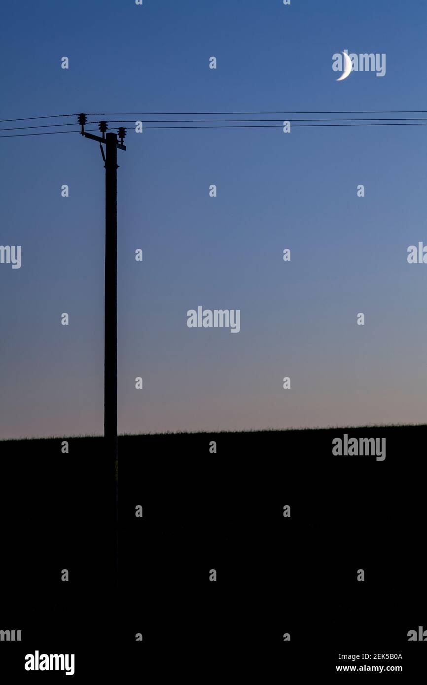 Crescent moon and telegraph pole at dusk Stock Photo