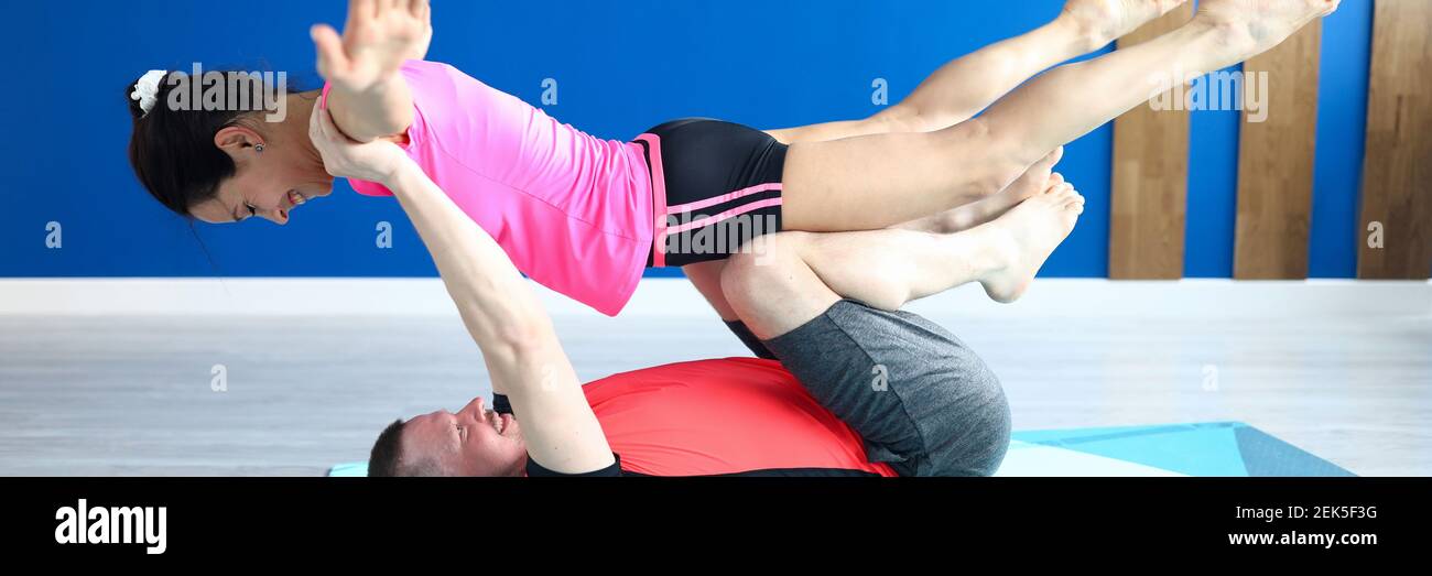 Man lie on his back on gymnastic rug in hall and do gymnastic exercise with woman in his arms. Stock Photo