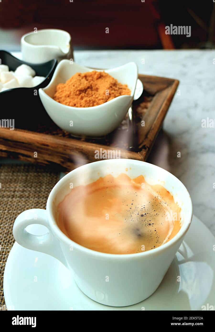 Cup of Hot Coffee with Smoke on the Table with Coffee Condiment Set in Background Stock Photo
