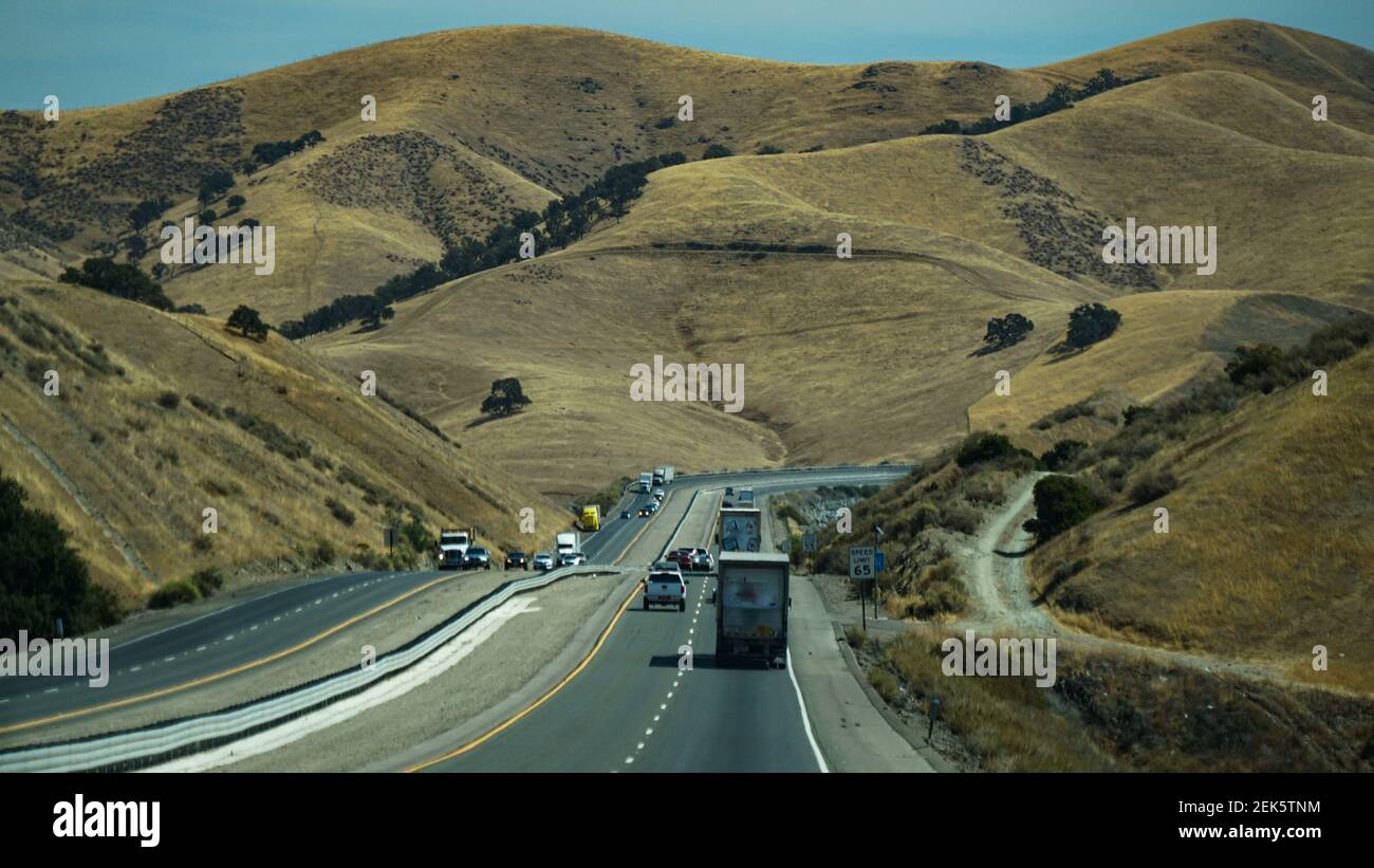 Vehicles driving through the afternoon sun in a hilly landscape in California, USA Stock Photo