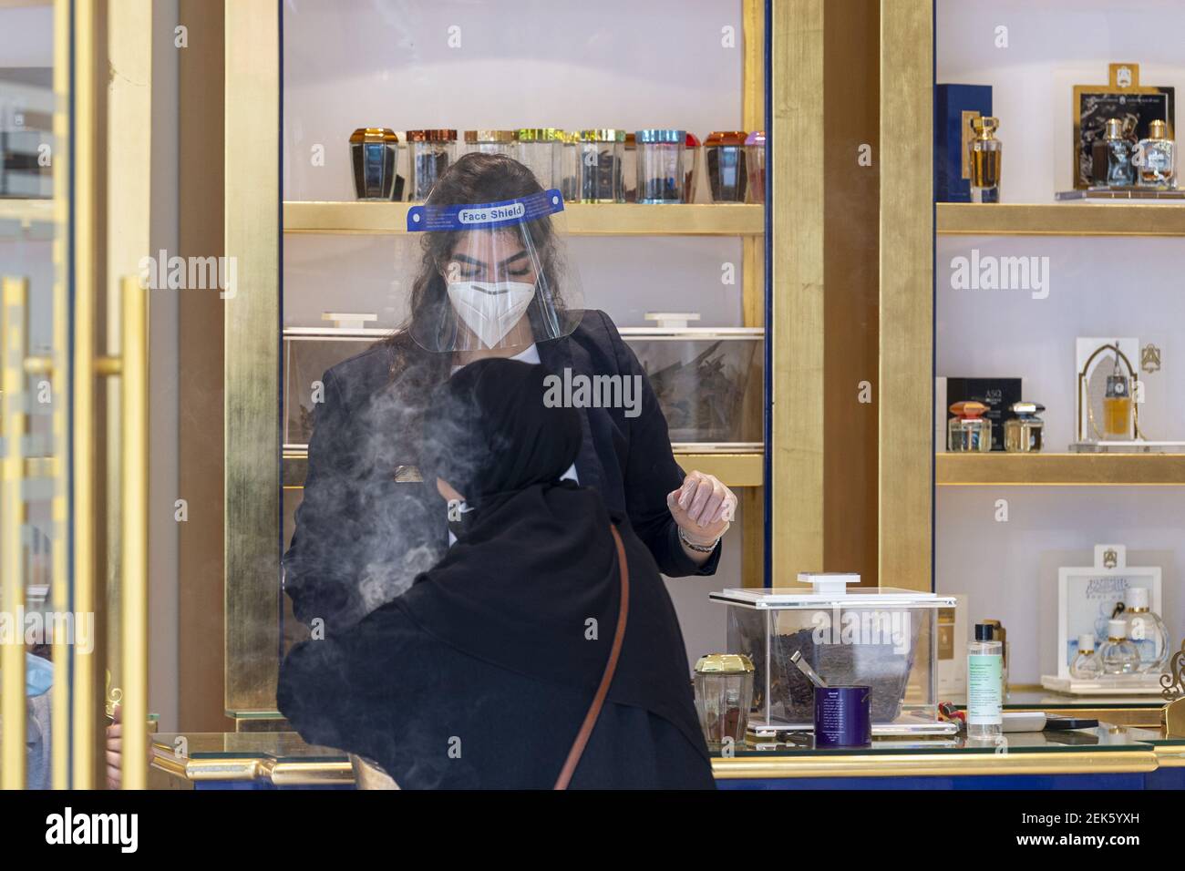 A worker of Arabian Oud perfume store wears a face shield as she serves