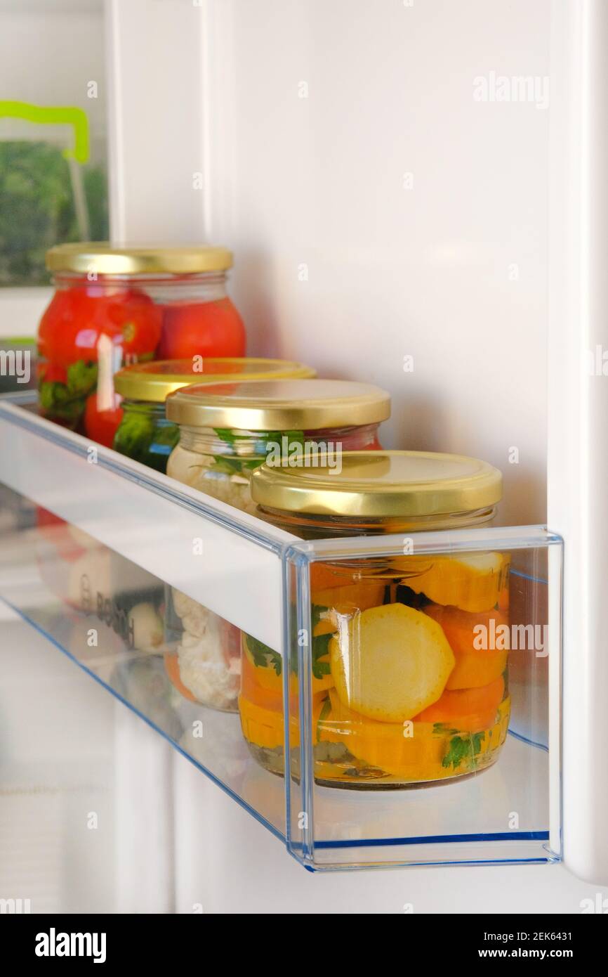 Variety glass jars homemade pickled vegetables on shelf of refrigerator