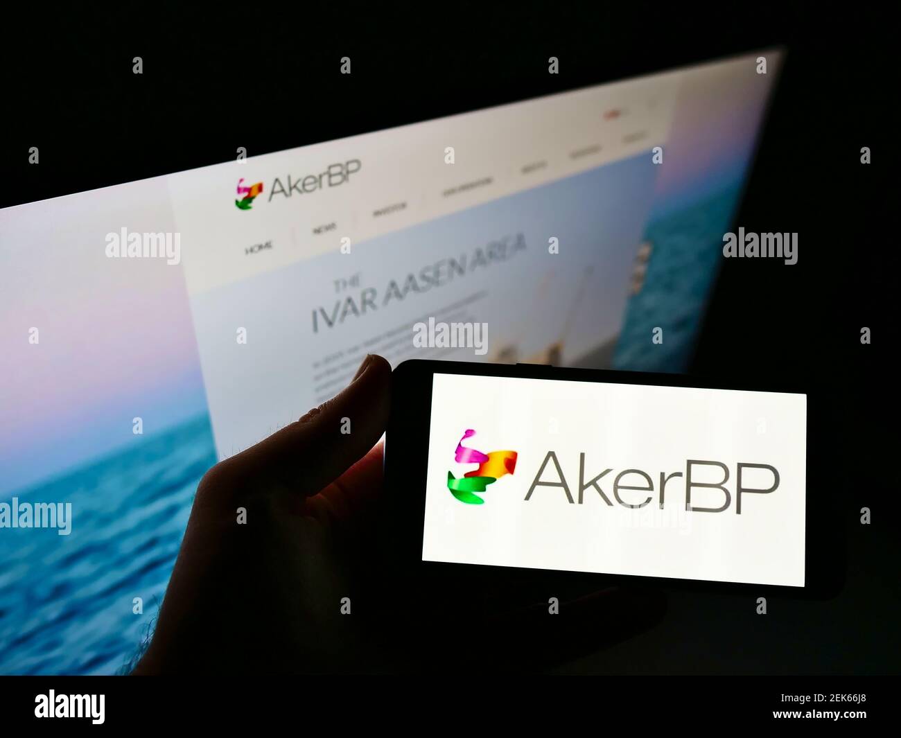 High angle view of person holding mobile phone with logo of Norwegian oil company Aker BP ASA on screen in front of web page. Focus on phone display. Stock Photo