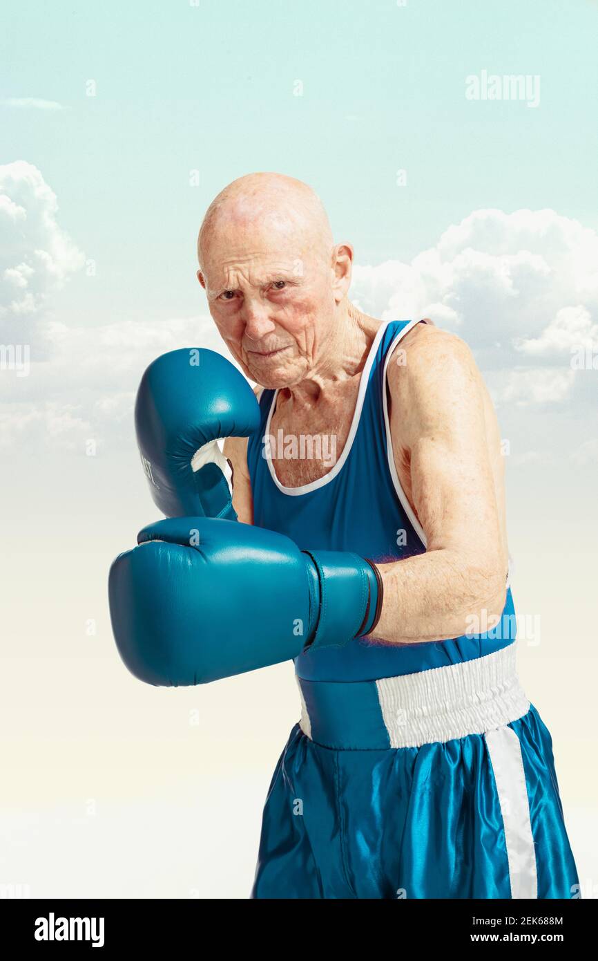 Senior man wearing sportwear boxing isolated on sky background ...