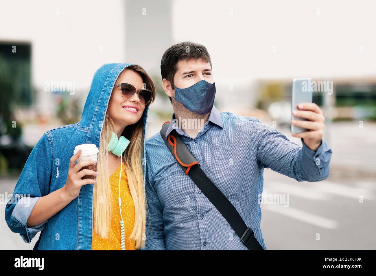 Happy boyfriend and girlfriend having fun taking selfie with face mask on city street Stock Photo