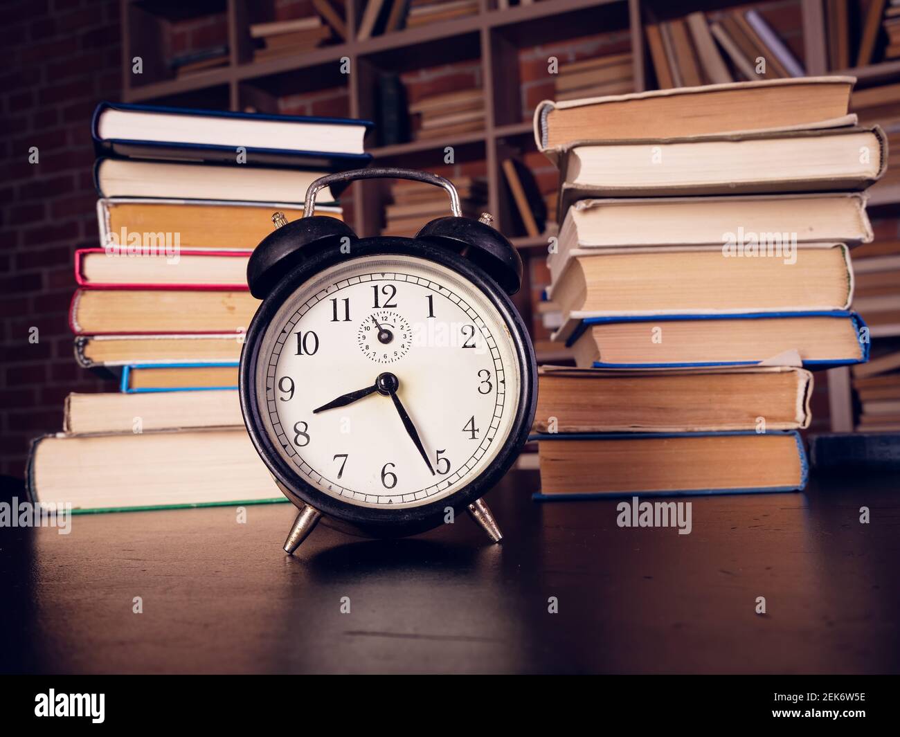 Time for learning concept. Alarm clock and lot of books in the library. Stock Photo