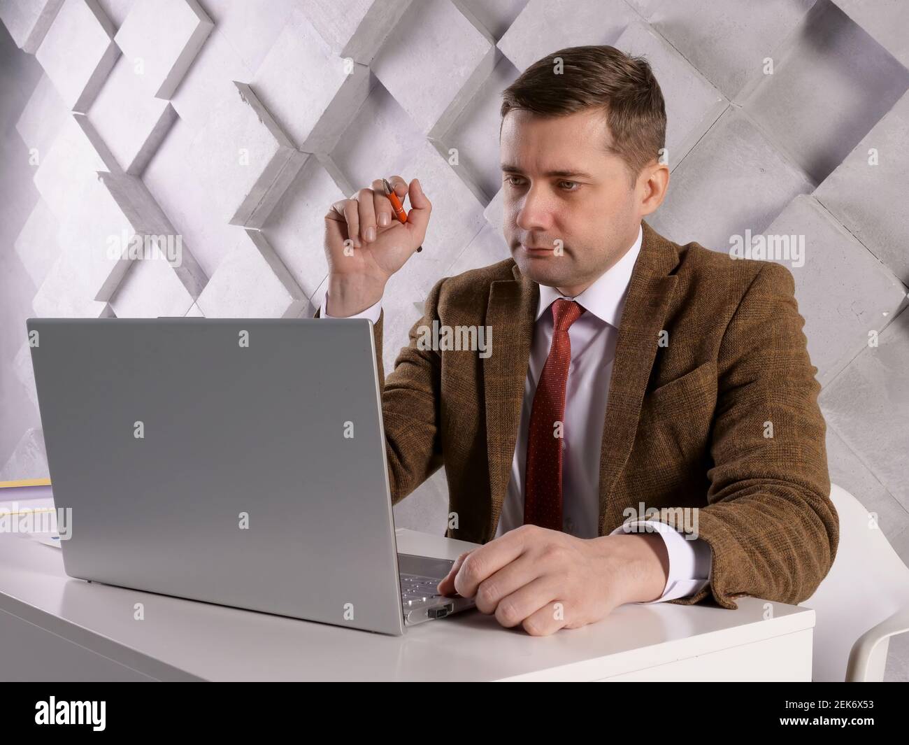 Manager with pen and papers reads data on a laptop screen. Stock Photo