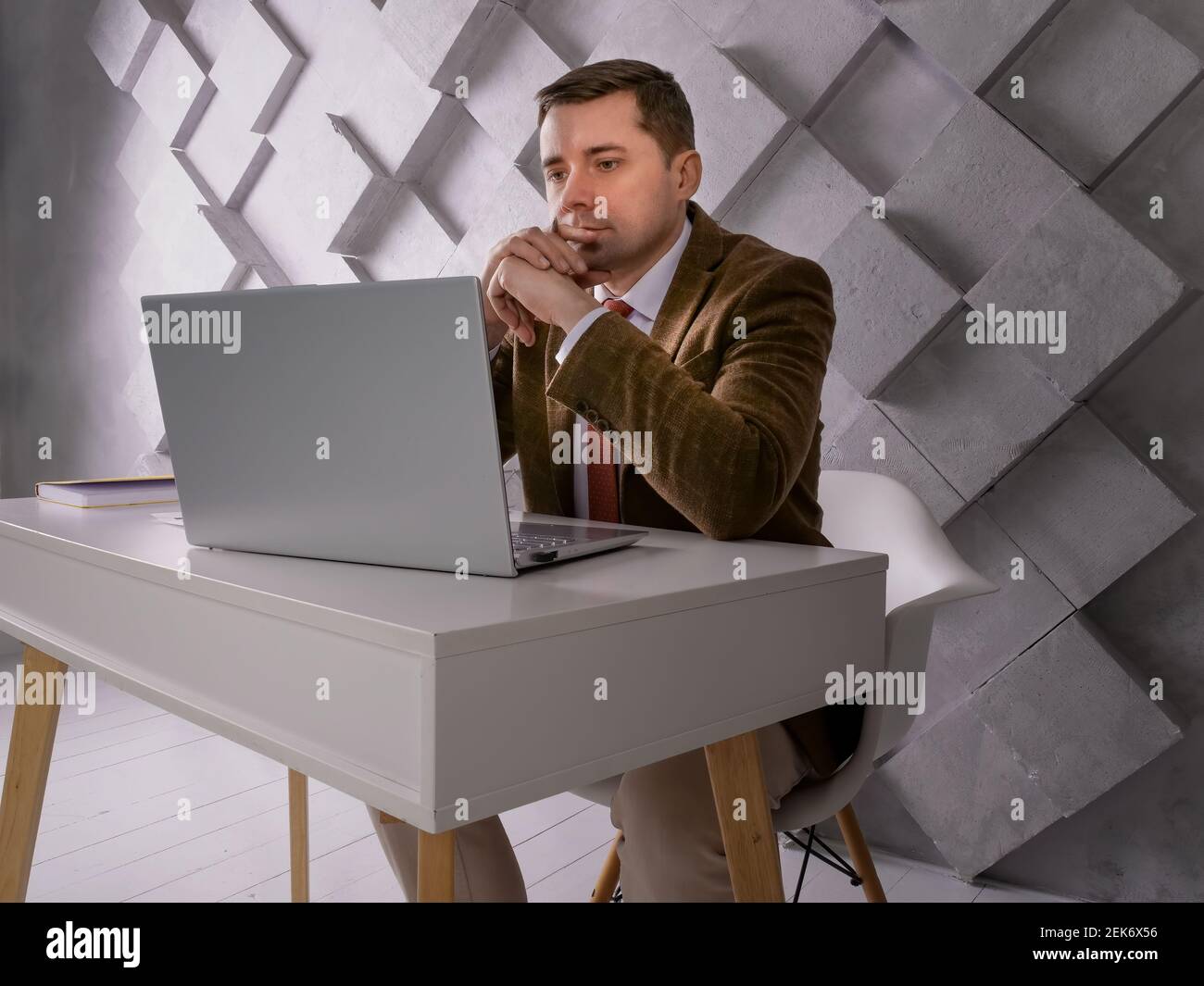 The man at the table looks at the laptop screen. Stock Photo