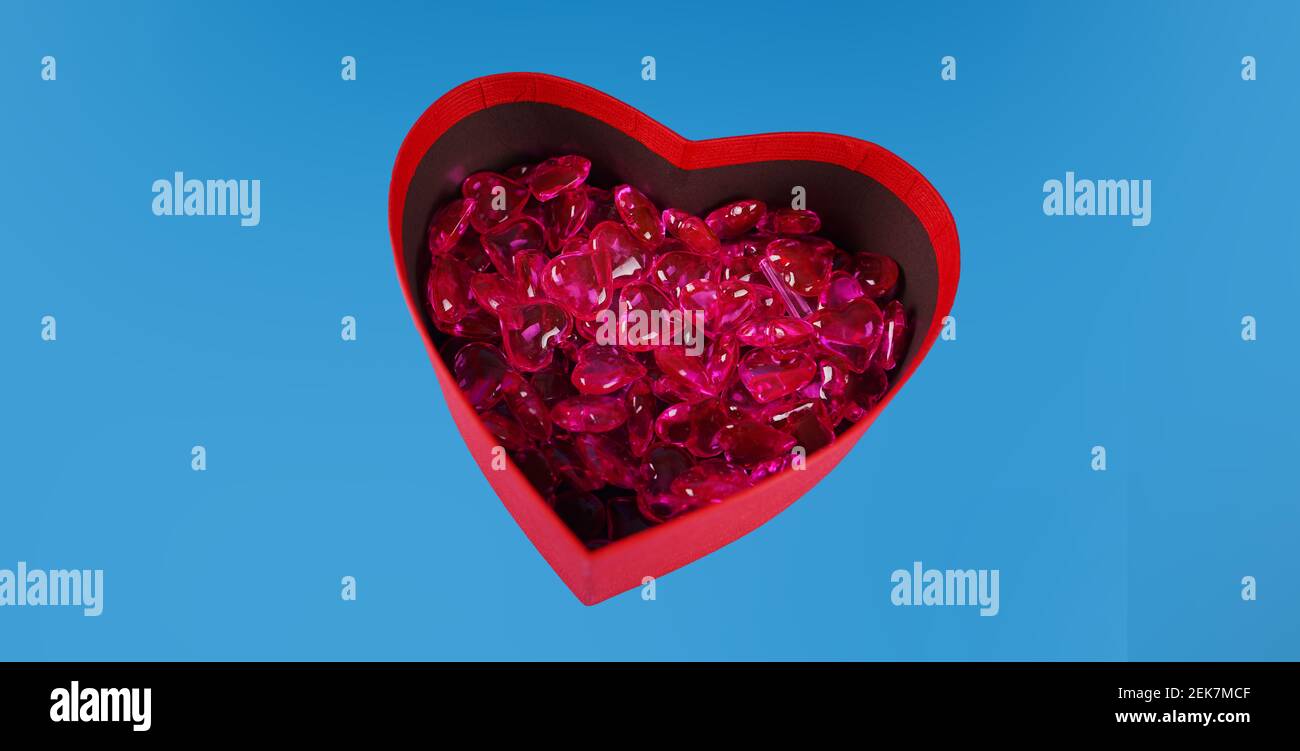 Close up of lots of hearts in red gift box in form of heart. Small red hearts in box for present on blue background. Concept of goodness, love and cha Stock Photo