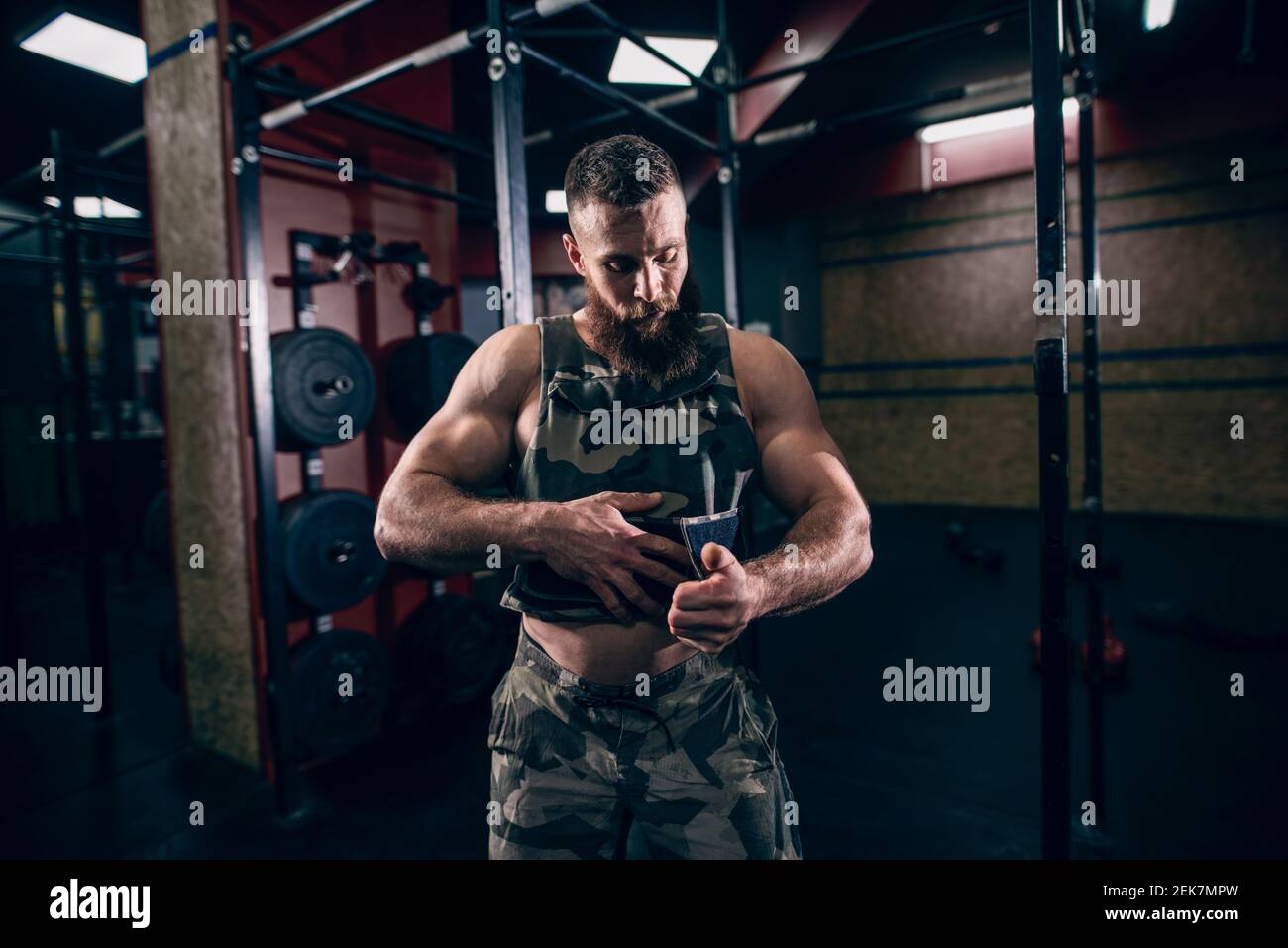 Muscular caucasian bearded man tightening up military style weighted vest  in crossfit gym. Weight plates and kettlebells in background Stock Photo -  Alamy