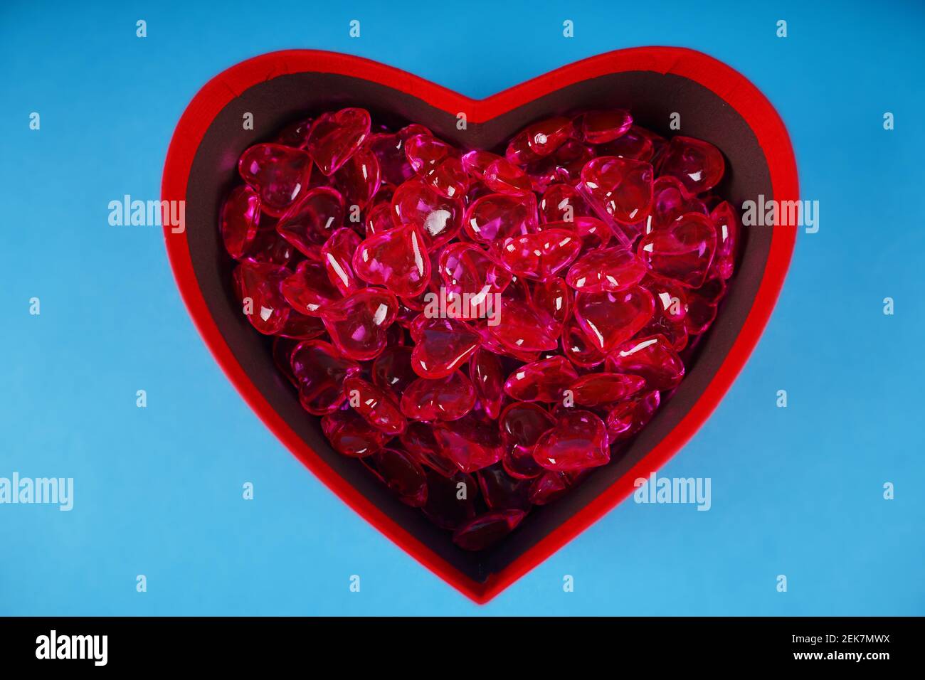 Close up of lots of hearts in red gift box in form of heart. Small red hearts in box for present on blue background. Concept of goodness, love and cha Stock Photo