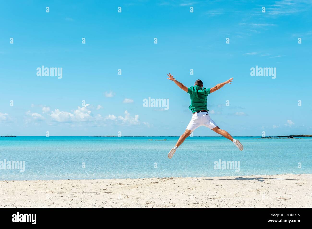 Happy young man jumping with outstretched arms on the beach. Summer vacation concept. Stock Photo