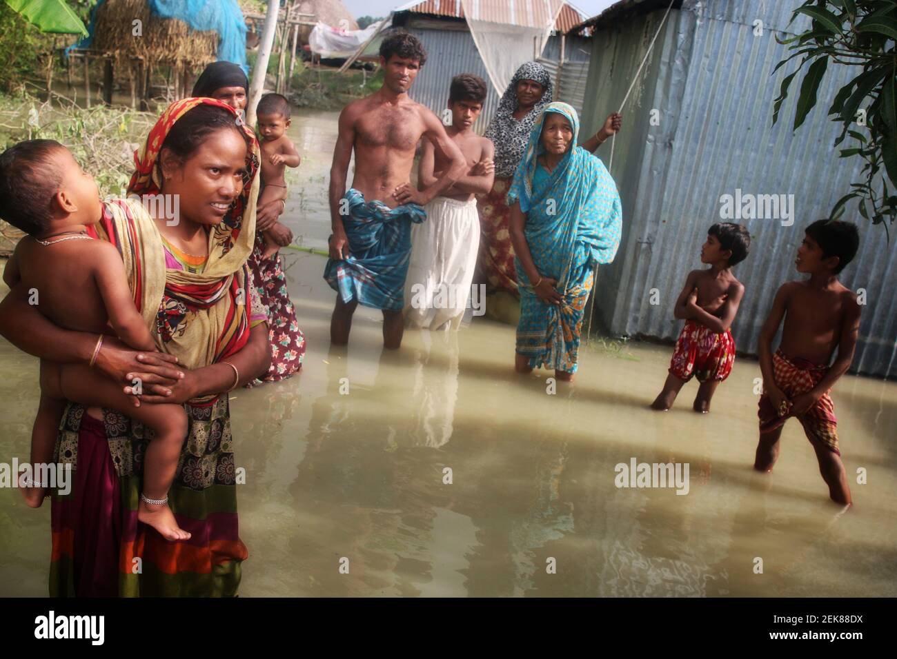 A family stands in flood water at a flooded area in Tangail. Around 129,000 villagers are marooned in and 3,686 hectares of croplands have been remaining submerged in Tangail due to floods. (Photo by Sultan Mahmud Mukut / SOPA Images/Sipa USA)  Stock Photo