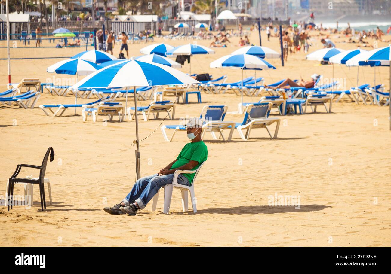 Las Palmas, Gran Canaria, Canary Islands, Spain. 23rd February, 2021. A man hiring sunloungers waits for customers as locals and the odd tourist bask on a quiet city beach in Las Palmas on Gran Canaria; a popular destination for many British holidaymakers. With no definite date for the return of foreign holidays, there was no good news for the beleaguered Canary Islands economy in Boris Johnson's recovery roadmap. Credit: Alan Dawson/Alamy Live News. Stock Photo