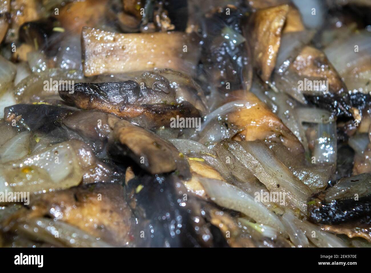 Wild mushrooms with onions are fried in a frying pan. Autumn harvest. Close-up, selective focus, surface texture. Stock Photo
