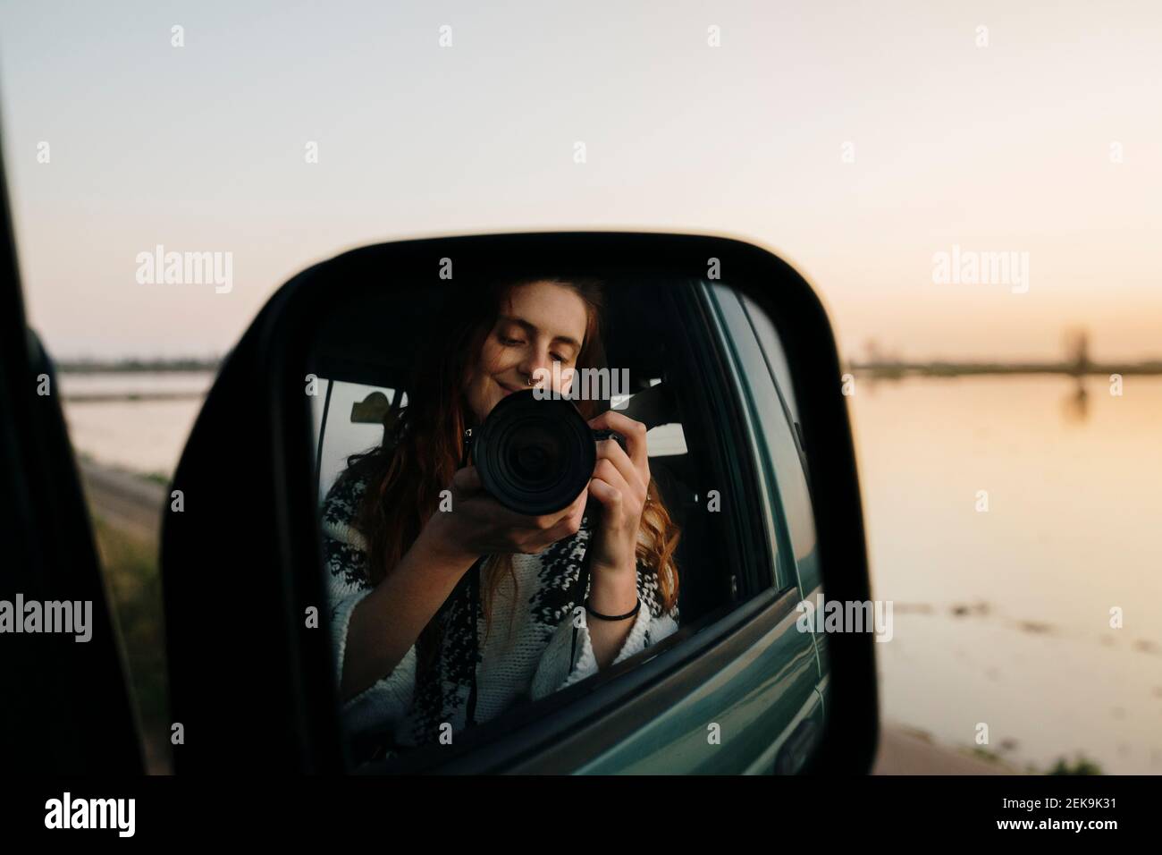 Young woman photographing self on side-view mirror reflection through camera at Ebro Delta Stock Photo