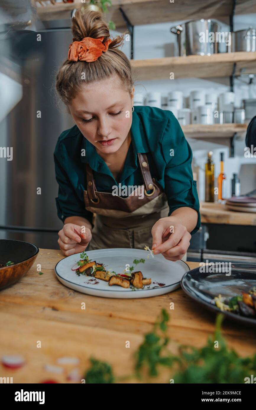 Young female chef garnishing dish while standing in kitchen Stock Photo
